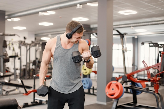 Young man in sportswear doing excercisses with dubells at gym