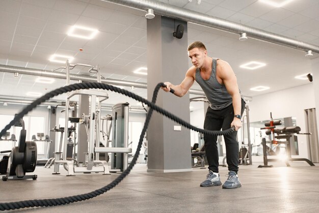 ジムで特別なロープでエクササイズをしているスポーツウェアの若い男