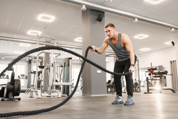Молодой человек в спортивной одежде делает упражнения со специальной веревкой в спортзале