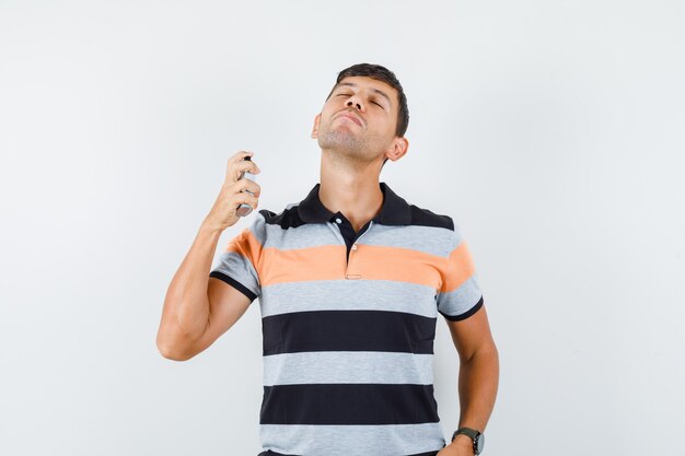 Young man spraying perfume in t-shirt and looking delighted