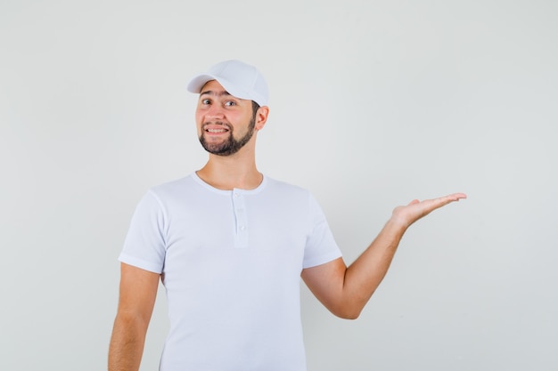 Free photo young man spreading palm aside in white t-shirt and looking cheerful. front view.