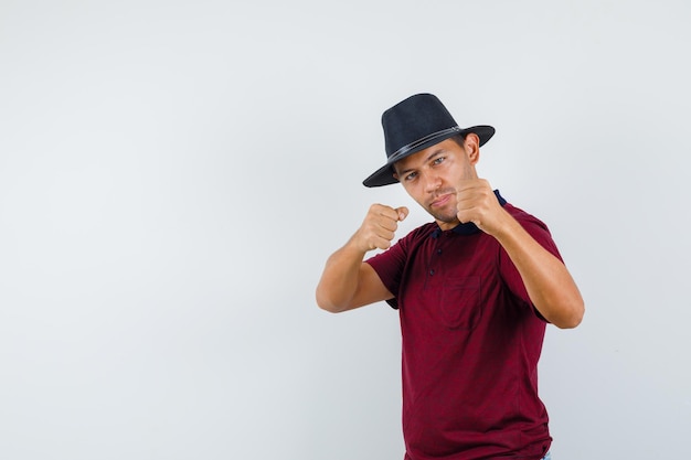 Молодой человек, стоящий в позе боксера в футболке, шляпе и выглядящий мощным, вид спереди.