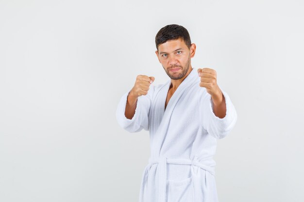 Young man standing in boxer pose in white bathrobe and looking powerful , front view.