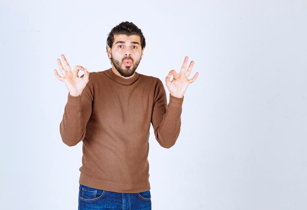 Young man standing in brown sweater showing ok gesture . High quality photo