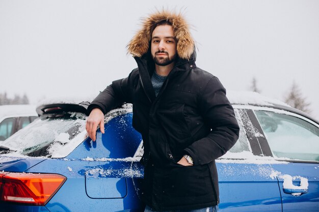 雪に覆われた車のそばに立っている若い男