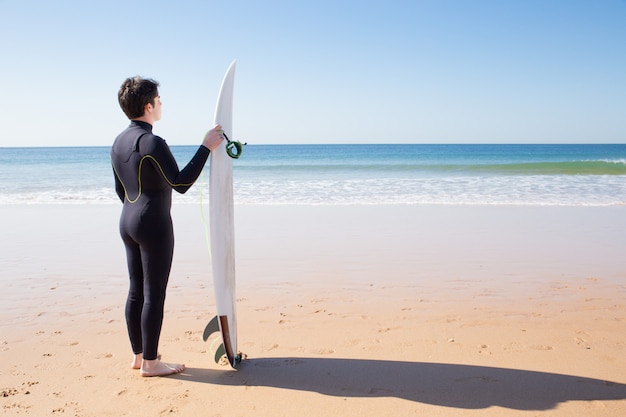 Young man standing by surfboard on summer beach