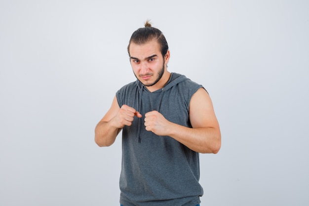 Young man standing in fight pose in sleeveless hoodie and looking confident. front view.