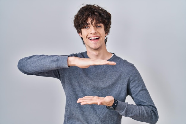 Free photo young man standing over isolated background gesturing with hands showing big and large size sign measure symbol smiling looking at the camera measuring concept