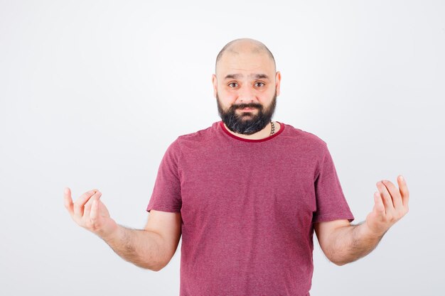 Young man standing in meditation position in pink t-shirt and looking serious , front view.