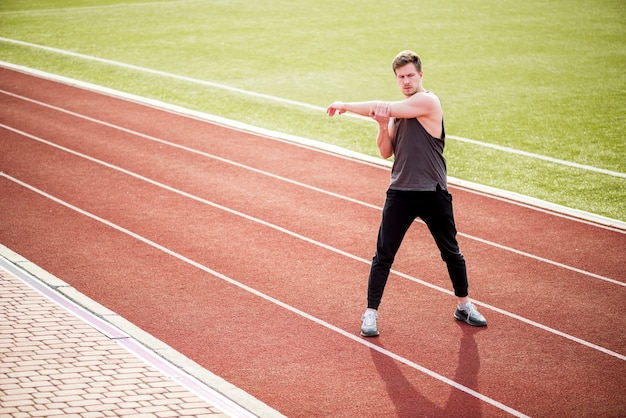 Young man standing on red race track stretching her hand