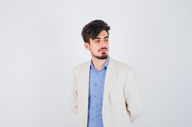 Young man standing straight and posing at front in blue t-shirt and white suit jacket and looking serious