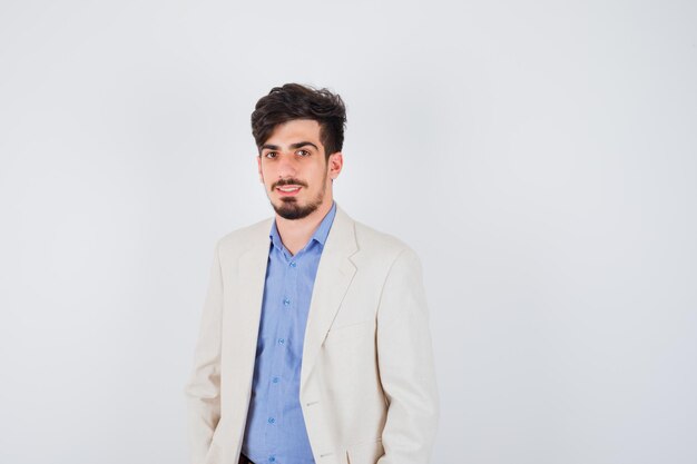 Young man standing straight and posing at front in blue t-shirt and white suit jacket and looking serious