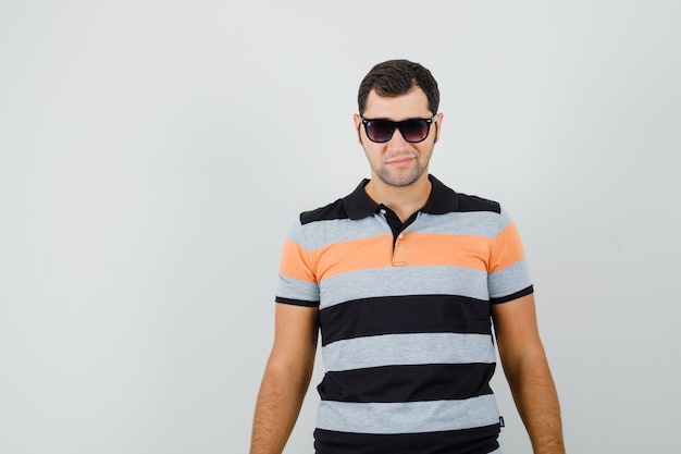 Young man standing in t-shirt,sunglasses and looking cool. front view. space for text