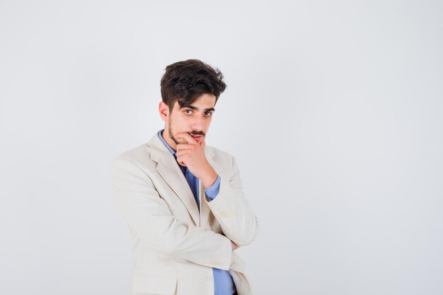 Young man standing in thinking pose in blue t-shirt and white suit jacket and looking pensive