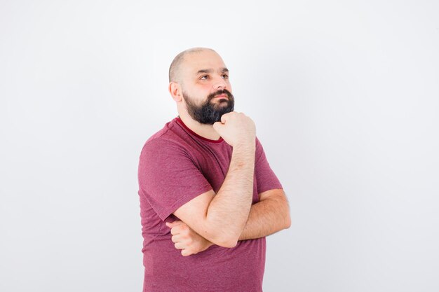 Young man standing in thinking pose in pink t-shirt and looking pensive. front view.