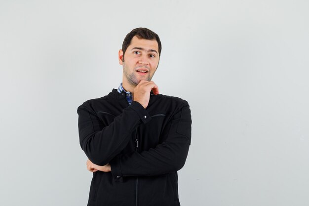 Young man standing in thinking pose in shirt, jacket and looking optimistic , front view.