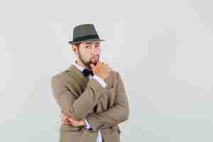 Free photo young man standing in thinking pose in suit, hat and looking sensible. front view.