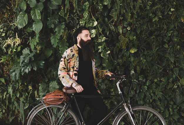 Young man standing with bicycle in front of green plants wall