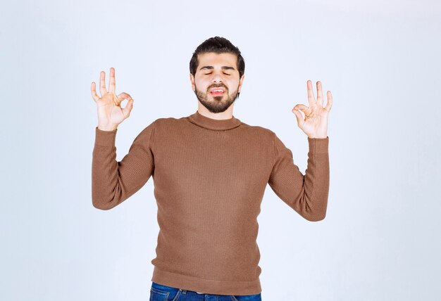 Young man standing with closed eyes and showing ok gesture . 