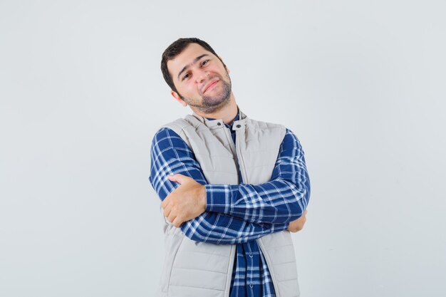 Young man standing with crossed arms in shirt,sleeveless jacket and looking calm. front view.