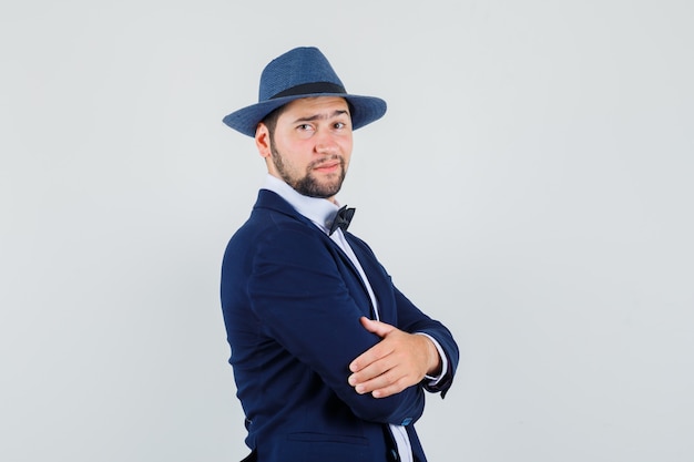 Young man standing with crossed arms in suit, hat and looking confident. front view.