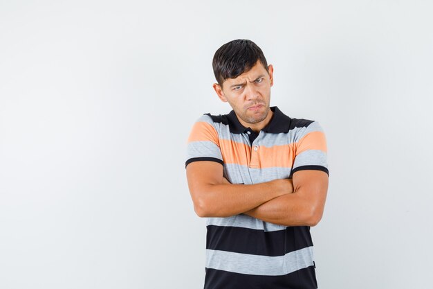 Young man standing with crossed arms in t-shirt and looking offended