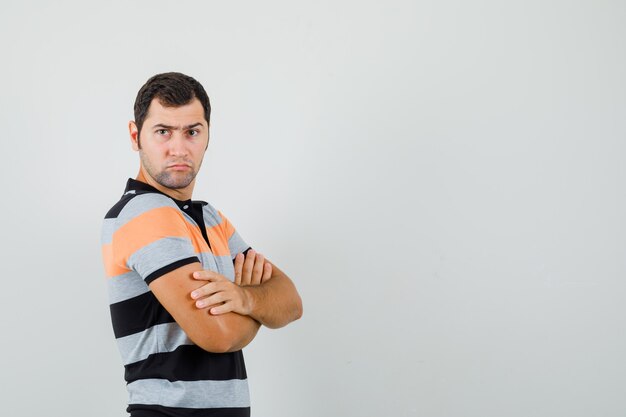 Free photo young man standing with crossed arms in t-shirt and looking serious. front view. free space for your text