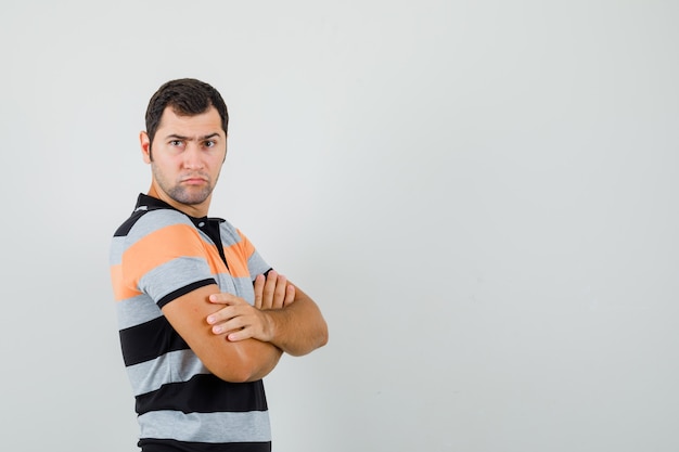 Tシャツを着て腕を組んで立って真剣に見える若い男。正面図。テキスト用の空き容量