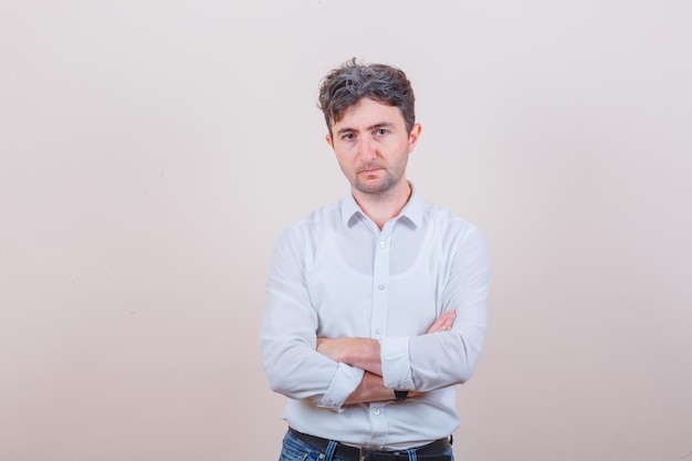 Free photo young man standing with crossed arms in white shirt, jeans and looking serious