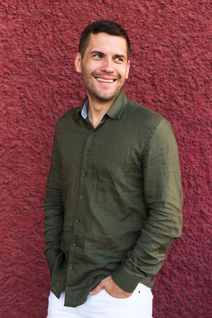 Free photo young man standing with hand in pocket near red wall