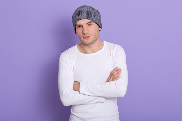 young man standing with hands folded wearing white casual shirt and gray cap. Copy space for advertisment or promotion text.