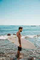 Бесплатное фото Молодой человек стоял с доской для серфинга в голубой воде