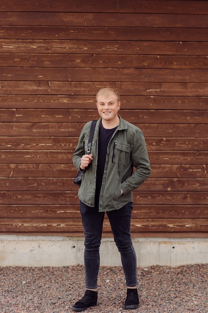 Young man standing next to a wooden wall