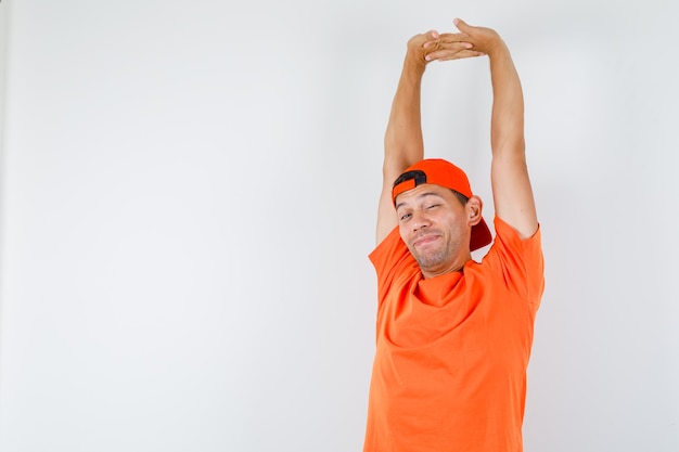 Young man stretching arms in orange t-shirt and cap and looking relaxed