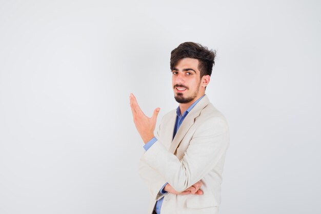 Young man stretching hand as holding something in blue shirt and white suit jacket and looking happy