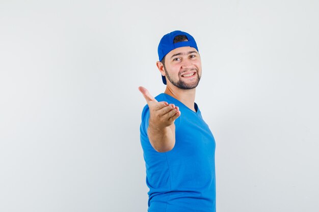 Young man stretching hand for shaking in blue t-shirt and cap and looking glad