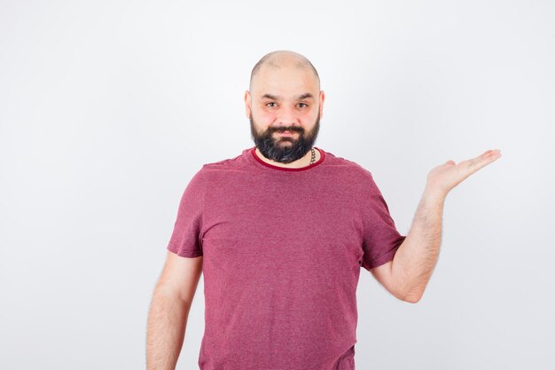 Young man stretching hands as holding something in pink t-shirt and looking optimistic , front view.