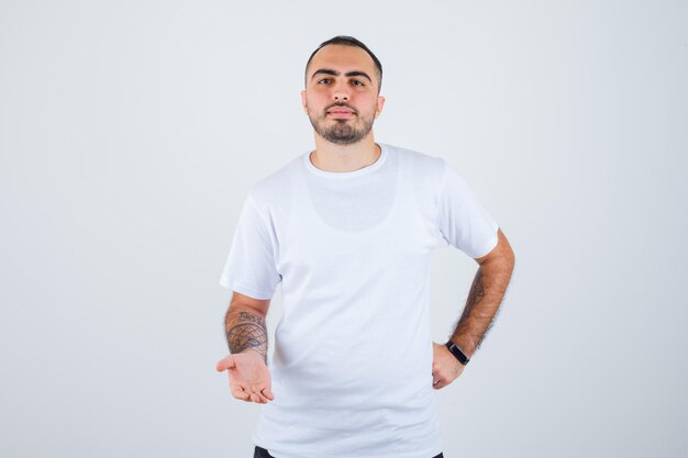 Young man stretching hands as holding something in white t-shirt and black pants and looking serious