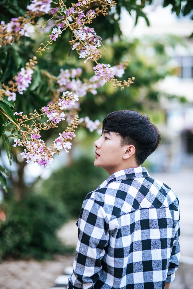 무료 Photo 줄무늬 셔츠를 입은 한 청년이 길가에 서서 꽃을 들고 있었다.