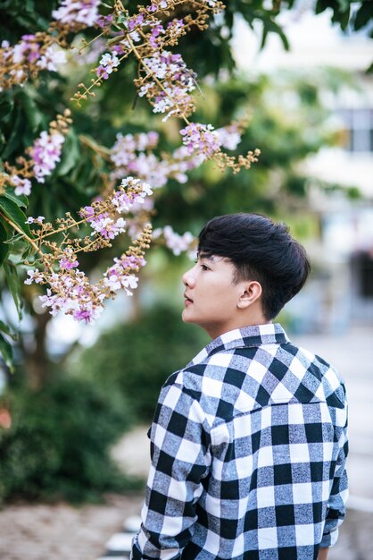 A young man in a striped shirt was standing on the roadside and holding the flower.