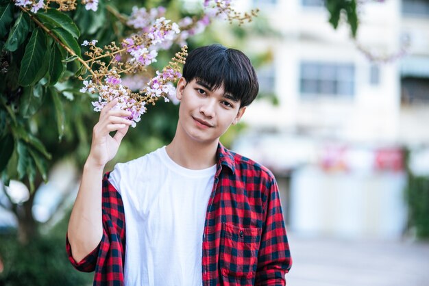 A young man in a striped shirt was standing on the roadside and holding the flower.