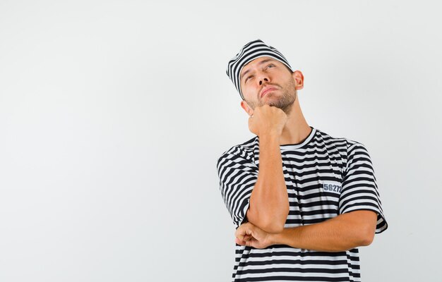 Young man in striped t-shirt hat looking up and looking pensive  