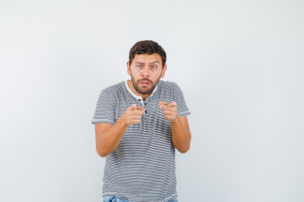 Молодой человек в полосатой футболке, указывая вперед и озадаченный, вид спереди.