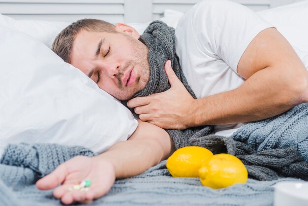 Young man suffering from cold lying on bed with pills in his hand