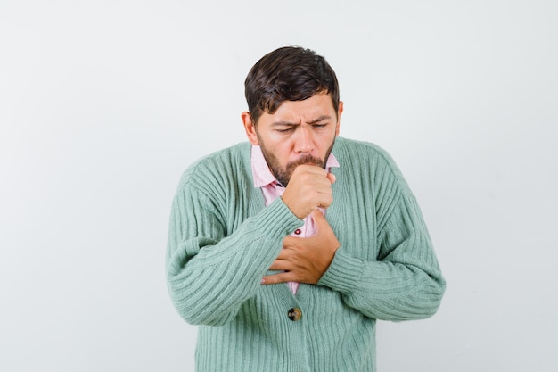 Young man suffering from cough in shirt, cardigan and looking sick , front view.