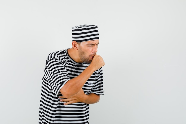 Young man suffering from cough in striped t-shirt, hat and looking sick.