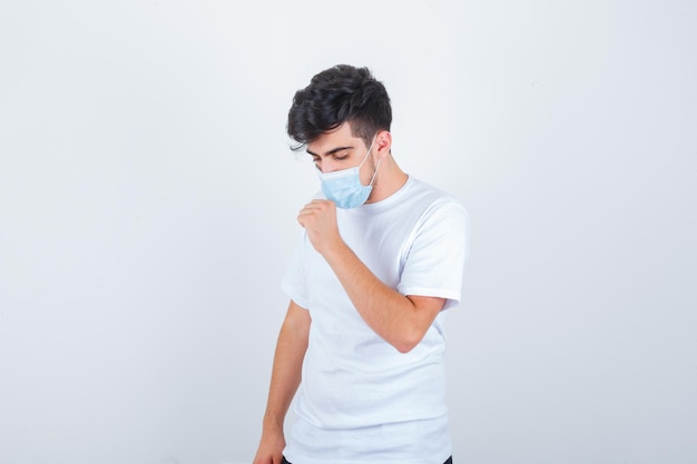 Young man suffering from cough in white t-shirt, mask and looking sick