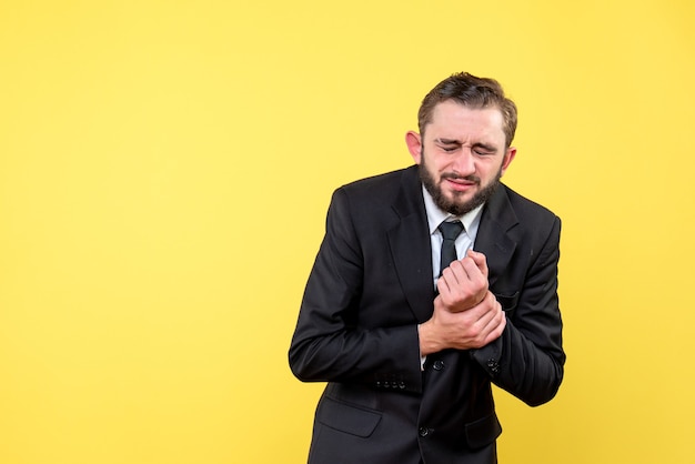 Young man suffering from hand pain while standing over yellow