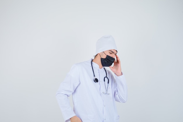 Young man suffering from headache in white uniform, mask and looking painful.