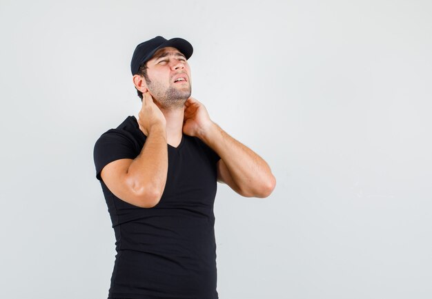 Молодой человек страдает от боли в шее в черной футболке